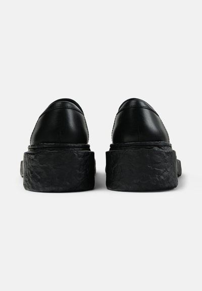 Black leather shoes with a textured, thick platform sole, featuring a rounded toe and smooth finish. Subtle stitching along the seams.