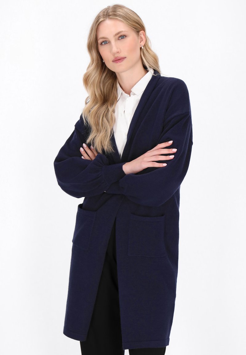 Marineblauer langer Cardigan aus weichem Strickmaterial, mit zwei vorderen Taschen und einer lässigen Passform mit gesenkten Schultern.