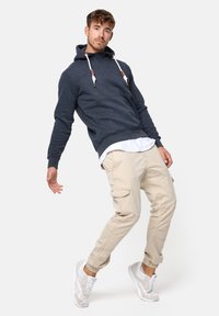 Sudadera azul oscuro con un acabado texturizado, cordones blancos, pantalones cargo beige y zapatillas ligeras con un diseño translúcido.