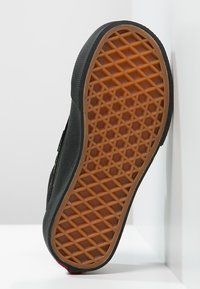 Black shoe sole with a textured rubber surface featuring a diamond-patterned grip and a tan-colored base.