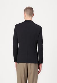 Musthave tekstuuriga must bleiser, millel on kohandatud siluett, lõhikutel kraed ja kaks esist pockets. Füüsiliselt nööbikeepe varrukatel.