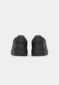Svarte sneakers med glatt skinnoverdel, rund form og teksturert gummisåle. Har preget merkevarelogo på hælen og minimalistisk design.