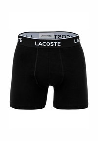 Czarne bokserki wykonane z miękkiego materiału o dopasowanym kroju. Posiadają kontrastowe białe logo Lacoste na elastycznym pasie.