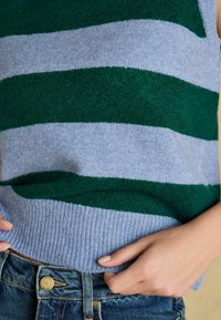 Nertinis marškinėliai su pakaitomis žaliais ir šviesiai mėlynais dryžiais. Rinktinė apačia ir minkšta medžiaga; dėvimi virš mėlynų džinsų.