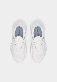 Ζευγάρι λευκών αθλητικών παπουτσιών Calvin Klein με λεπτομέρειες από δίχτυ, κορδόνια και ορατό όνομα της μάρκας στις εσωτερικές σόλες και τη γλώσσα, από πάνω.