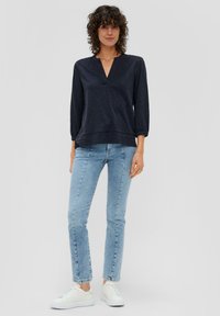 Marineblauer Pullover mit V-Ausschnitt und Dreiviertelärmeln, kombiniert mit hellblauen Skinny-Jeans und weißen Sneakers. Weiche Textur, lässiger Schnitt.