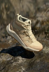 Pantof de drumeție de culoare bej, cu un partea superioară texturată, șireturi și o talpă căptușită. Dispune de o talpă din cauciuc și un logo subtil pe lateral.