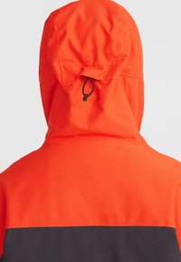 Chaqueta con capucha naranja y un panel inferior negro, con ajuste de cordón en la capucha y una textura de tejido suave y resistente al agua.