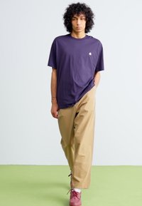 Purple oversized t-shirt, beige wide-leg pants, and maroon shoes. Simple design with a front logo detail. Smooth fabric and relaxed fit.