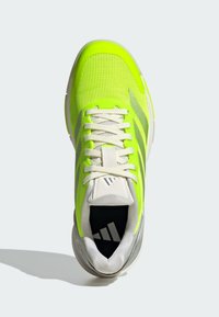 Neon yellow athletic shoe with a textured mesh upper, white laces, and a grey sole. Features a logo on the tongue and a grey accent near the heel.