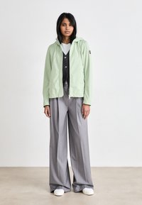 Világoszöld, cipzáros kapucnis dzseki, alatta fekete gombos mellény, szürke, széles lábú nadrág és fehér sportcipő. Egyszerű dizájn, puha szövet textúra.