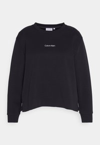 Sudadera negra de cuello redondo hecha de tejido suave, con un logo blanco de "Calvin Klein" en el centro. Puños y dobladillo acanalados, corte relajado.
