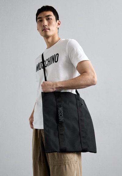 Black tote bag with two sturdy straps, featuring the "Moschino" logo in raised lettering along the side, made of durable material.
