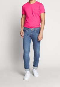 Camiseta de algodón rosa ajustada con cuello redondo, combinada con jeans de denim azul claro y zapatillas blancas. Puños de los jeans doblados.