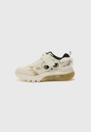 White sneaker with owl design, featuring black accents, a glittery gold side panel, adjustable strap, soft fur accents, and a translucent sole.