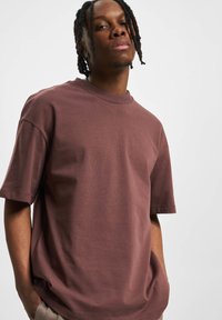 Camiseta de algodón marrón con cuello redondo, mangas cortas y un corte relajado. La tela tiene una textura suave y un diseño minimalista.