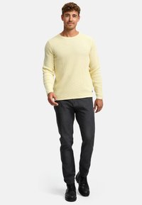 Maglione giallo a coste con maniche lunghe, scollo a girocollo, abbinato a jeans grigio scuro e stivaletti neri alla caviglia. Design semplice e informale.