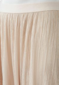 Gelaagde rok in lichtroze stof, met een zachte elastieken tailleband en een glanzende textuur met metalen draden, die verticale lijnen creëert.