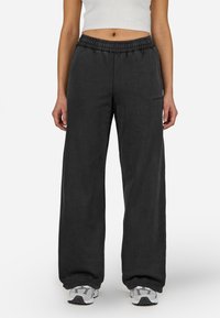 Μαύρες φαρδιές φόρμες από μαλακό ύφασμα. Διαθέτουν ελαστική μέση και λεπτομέρεια λογότυπου στο πλάι. Συνδυάζονται με γκρι αθλητικά παπούτσια.