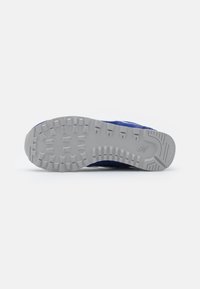 Baskets de sport bleues avec une semelle en caoutchouc gris texturé, dotée de crampons multidirectionnels pour une adhérence optimale et d'un embout renforcé.
