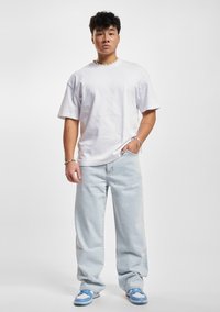 Camiseta blanca de algodón con corte relajado, combinada con unos jeans holgados de color azul claro y zapatillas azul y blancas, presentando una textura sutil y sin patrones.