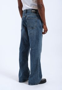 Lösa blå denimjeans med blekt tvätt, fem fickor och en svart etikett vid bakre midjan. Texturerad tyg med synlig sömnad.