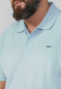 Lichtblauwe polo van textiel, met een twee knoopsluiting en een klein geborduurd logo op de borst.