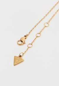 Κολιέ με χρυσή αλυσίδα που διαθέτει κούμπωμα σε σχήμα αστακού και τριγωνικό μενταγιόν με ανάγλυφο το λογότυπο "GUESS".