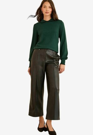 Skovgrøn sweater med krave, parret med højtaljede, vide sorte læderbukser. Modellen har sorte slingback sko på.