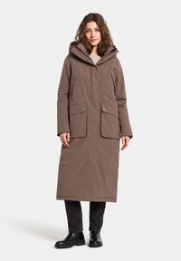 Bruine lange buitenjas met capuchon, voorzien van twee voorzakken, een ritsluiting en een gladde, gestructureerde afwerking.