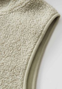Fleece-Weste in Creme mit einer strukturierten, plüschigen Oberfläche. Verfügt über einen glatten grauen Besatz um die Armausschnitte, der die kontrastierenden Materialien betont.