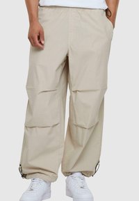 Beige cargo bukser lavet af letvægtsstof, med sidelommer, elastisk talje, justerbare mansjetter og en afslappet pasform.