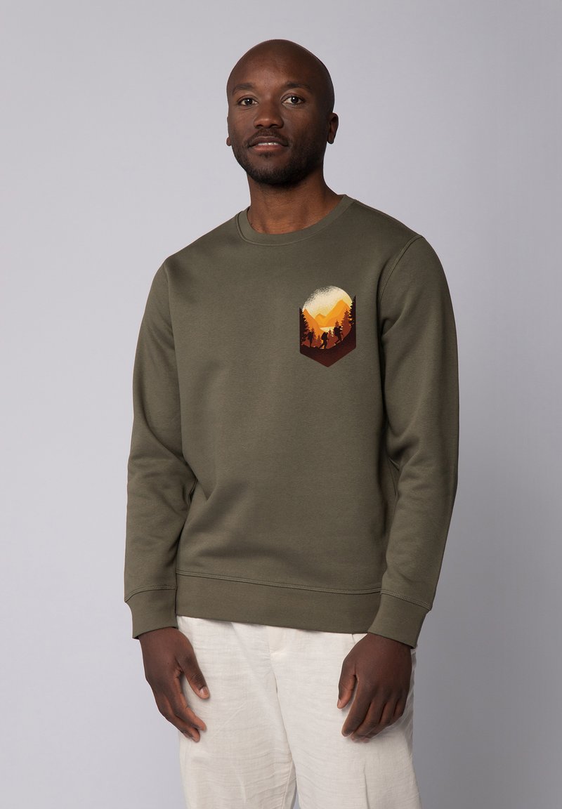 Olijfgroene sweater gemaakt van zachte stof. Heeft een geometrische graphic in warme kleuren die bergen en bomen op de borst afgebeeld.