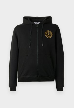 Svart hettejakke med glidelås, frontlommer, justerbar hette og gult sirkulært "Versace Jeans Couture"-logo på venstre bryst.