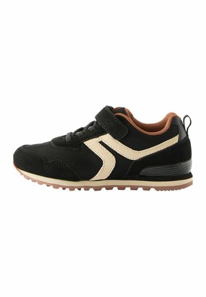 Chaussure de sport noire avec une tige en mesh et des accents en daim, une bande latérale beige, des bandes Velcro et une semelle en caoutchouc brun.