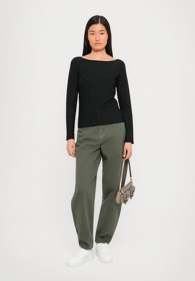Maglietta nera a maniche lunghe con motivo testurizzato, abbinata a pantaloni larghi verde oliva e sneakers bianche, mentre tiene una piccola borsa testurizzata.