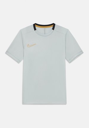 Svetlo siva športna majica s kratkimi rokavi z črnimi in zlatimi poudarki na ovratniku ter zlatim logotipom Nike Swoosh na levem prsnem delu.