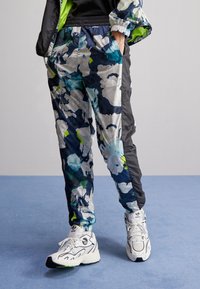 Mønstret track pants i flere farver med blomsterdesign i blå, grøn og hvid, kontrasterende sorte sider og elastiske manchetter. Brandlogo synligt.