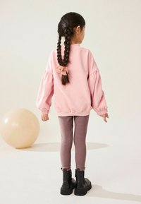 Felpa rosa chiaro con maniche a sbuffo, impreziosita da un fiocco sul retro, abbinata a leggings mauve a costine e stivaletti neri alla caviglia.