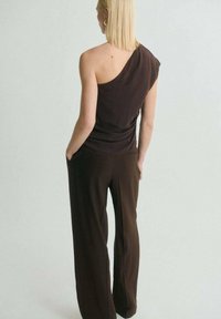 Top tank asimmetrico marrone abbinato a pantaloni larghi marroni. Tessuto liscio con una vestibilità comoda, che mette in mostra un design minimalista.