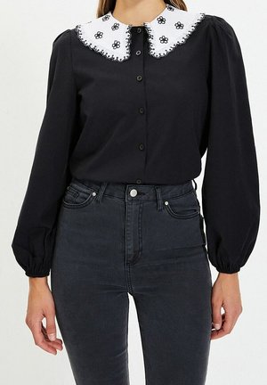 Czarna bluzka z długim rękawem z białym falowanym kołnierzykiem wyszywanym czarnymi kwiatami, połączona z ciemnymi jeansami z wysokim stanem.