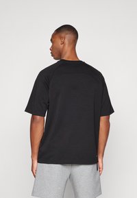 Μαύρη κοντομάνικη μπλούζα με στρογγυλή λαιμόκοψη και ραγλάν μανίκια. Λείο υλικό με λεπτή καμπύλη ραφή στο πίσω μέρος.