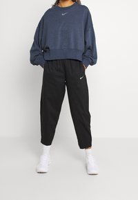 Tmavě modrá mikina s kulatým výstřihem a volným střihem. Černé kalhoty s elastickým pasem. Oba kousky mají bílé logo Nike. Bílé tenisky.