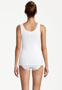 Camisetta in cotone bianco con texture a pois, spalline larghe e scollatura rotonda, abbinata a biancheria intima bianca coordinata.