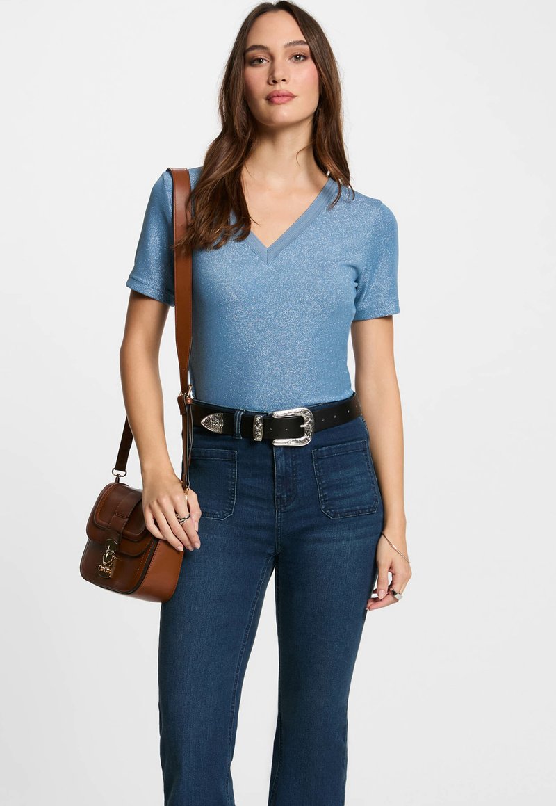 Top blu, a maniche corte, con scollo a V e una leggera lucentezza, abbinato a jeans decolorati blu scuro a vita alta e una borsa a spalla marrone con pattina.