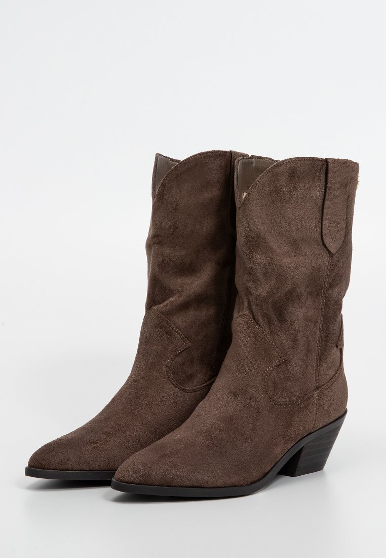 Stivali da cowboy in suede marrone con punta affusolata, altezze medie dello stivale e dettagli di cucitura sottili; il tacco basso impilato aumenta la stabilità.