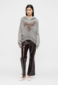 Γκρι φούτερ με κουκούλα με γραφικό αετού και ραμμένες λεπτομέρειες, σε συνδυασμό με λαμπερό, σκούρο μπουργουνδί παντελόνι και κρεμ μυτερά mules.