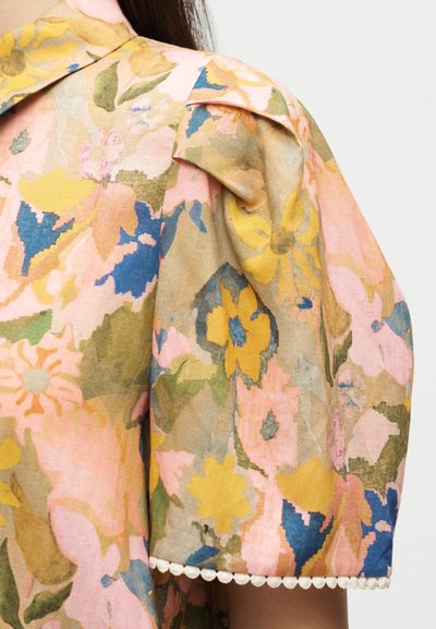 Κοντινή λήψη ενός κοντού φουσκωτού μανικιού με λουλουδάτο μοτίβο σε ροζ, κίτρινο, μπλε και πράσινο χρώμα και μια μικρή λευκή φούντα στην άκρη.