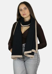 Écharpe noire avec bordure métallique dorée. Tissu doux et texturé qui se drape élégamment autour du cou. Tenue décontractée avec un décolleté plongeant et un jean taille haute.