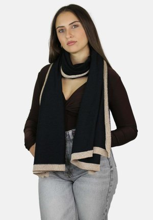 Zwarte sjaal met metalen gouden rand. Zachte, textuurrijke stof valt elegant om de nek. Casual outfit met een diepe halslijn en high-waisted jeans.